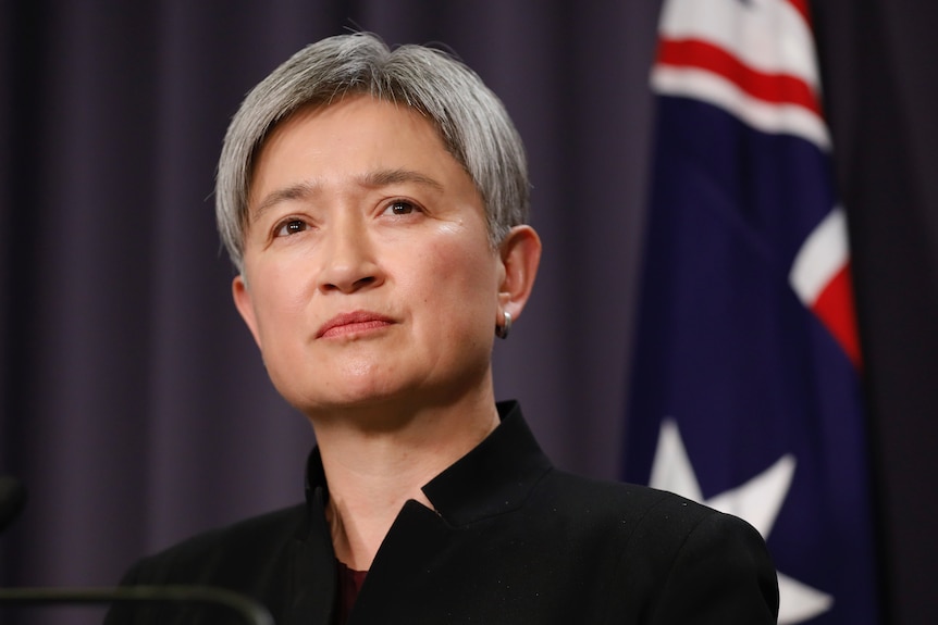 Penny Wong speaks with an Australian flag behind her