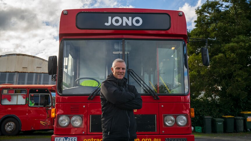 A man stands in front of a big red bus,