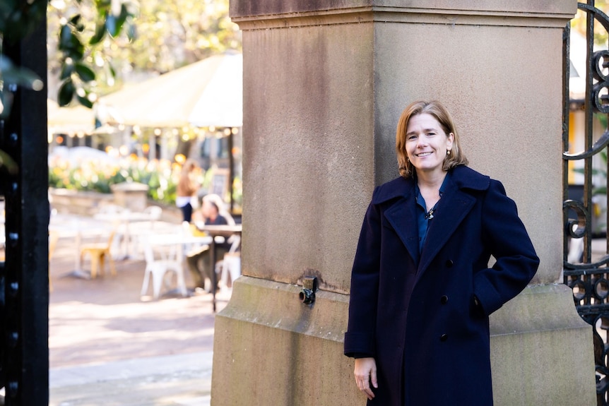 Dr Anna Brooks wears a winter coat standing in front of a cafe smiling.