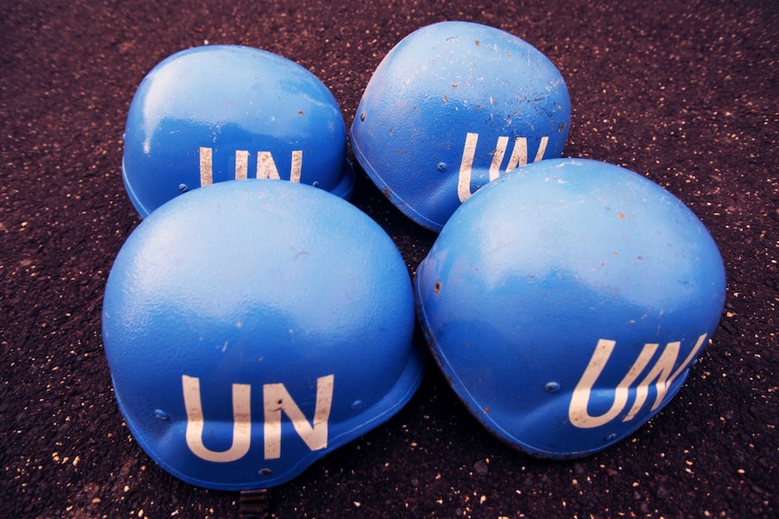 Four blue United Nations helmets sit on the ground.