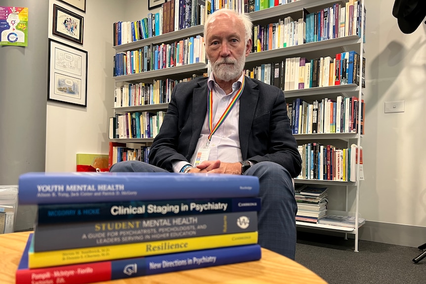 A man with grey hair seated behind a stack of books