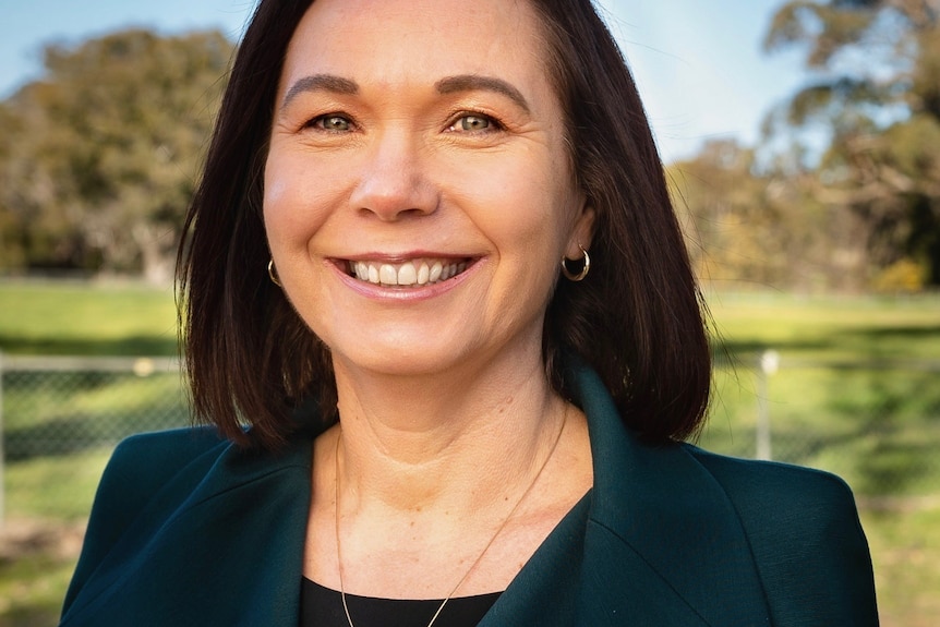 Woman wearing dark green jacket with short brown hair smiling.