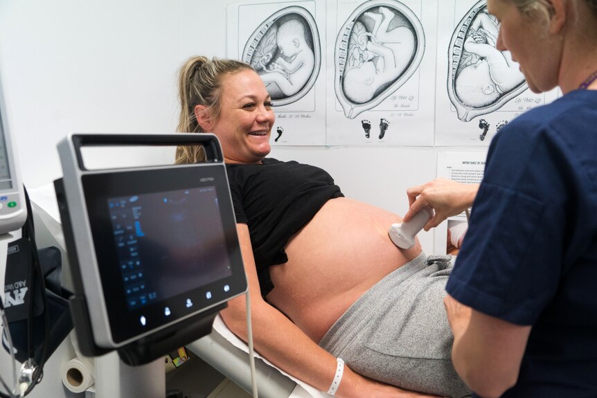 A pregnant woman smiling as she lies in a hospital bed while receiving an ultrasound.