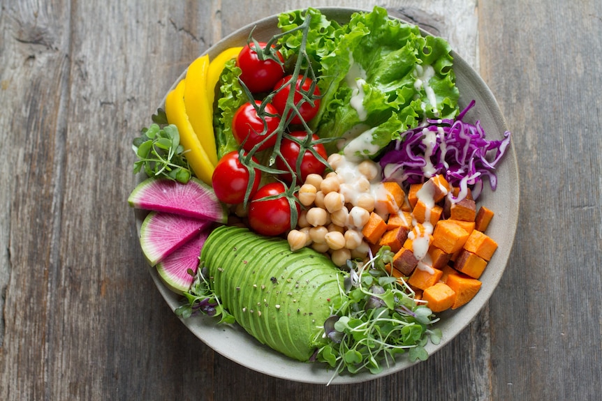 A bowl of salad: red tomatoes, green lettuce, avocado and sprouts, purple cabbage, yellow capsicum, chickpeas