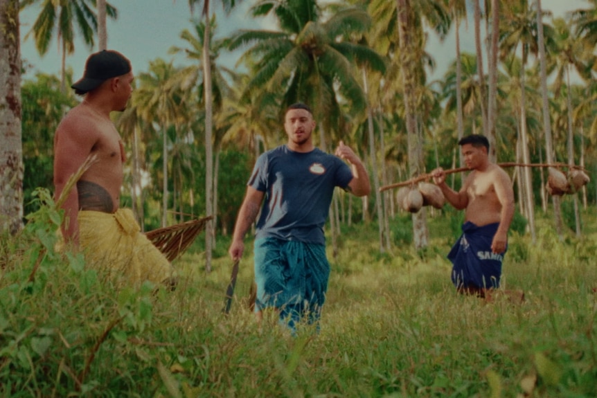 Three men work in green field full of coconut trees wearing ie lava lavas. 