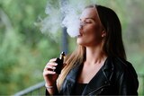 A close-up of a woman vaping, blowing out a big cloud of smoke.
