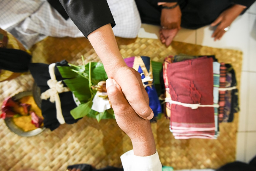Hands shaking above dowries including fabric and flowers. 