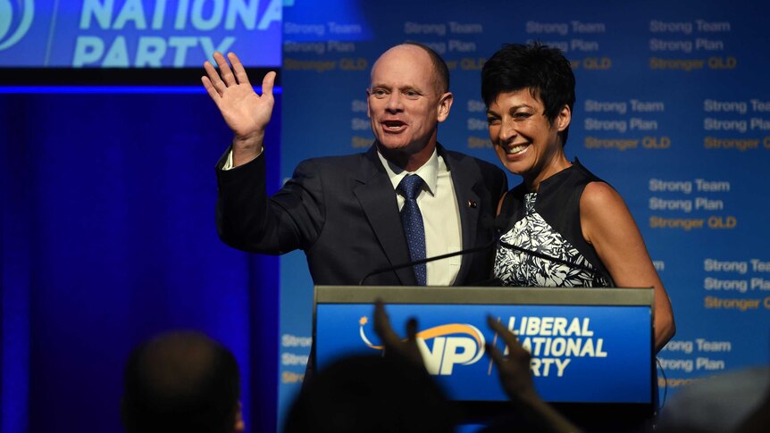 A man and woman stand at a lectern, the man is waving.