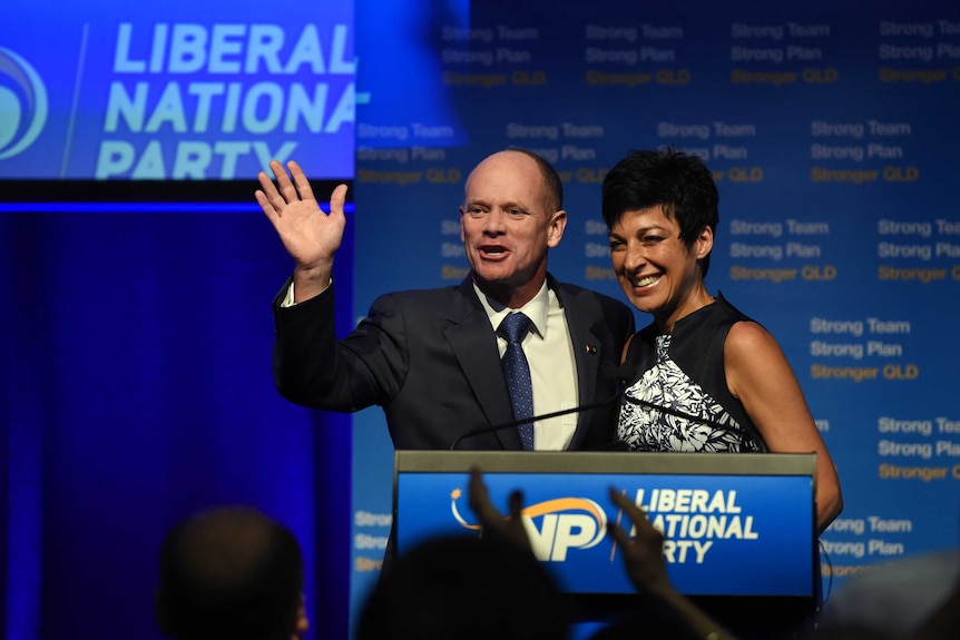 A man and woman stand at a lectern, the man is waving.