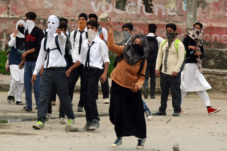 School students wearing their uniforms, backpacks and masks throw rocks at Indian security officers in Kashmir.