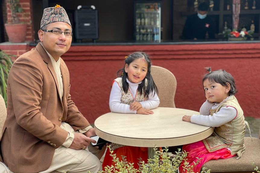 Pranab Shrestha sits at an outdoor table with his daughters.