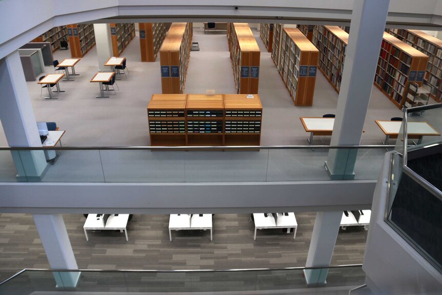 Shot looking down on empty rows of bookshelves and desks in a library.