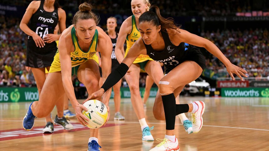 Two netball opponents stoop to get their hands on the ball in a contest.