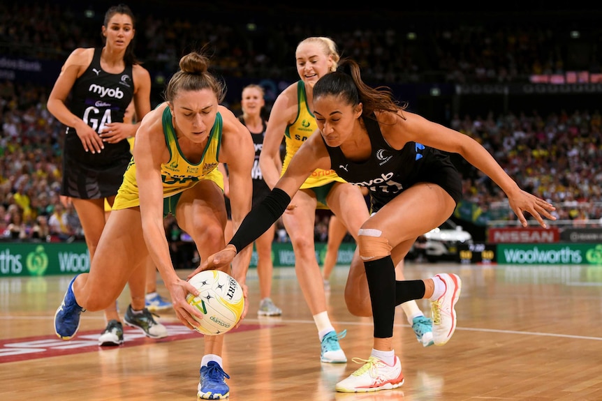Two netball opponents stoop to get their hands on the ball in a contest.