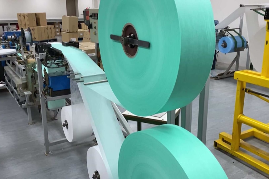 Blue-green material runs through a machine to make medical masks