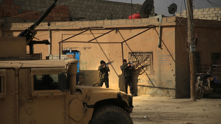 Two men with big guns standing outside a building near heavy artillery 