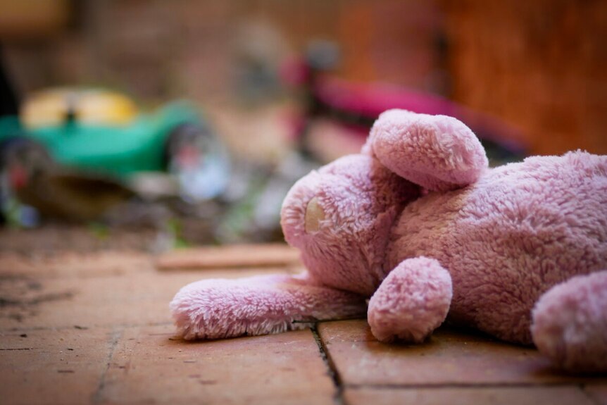 A pink bunny rabbit child's toy sitting on the ground with other toys blurred in the background.
