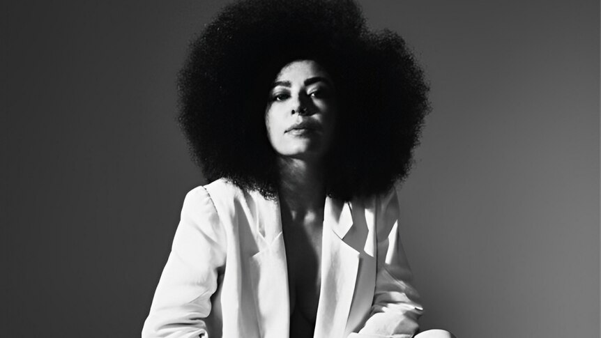 A monochrome photo of Vanessa Moreno in a white suit; she's sporting an afro and is looking at the camera