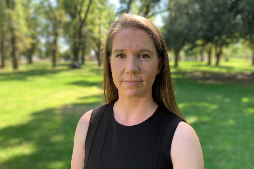 Woman stands in park, looking at the camera