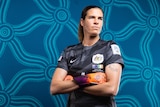 Matildas goalie Lydia Williams poses for a portrait in a black jersey. She is looking into the distance with her arms crossed.
