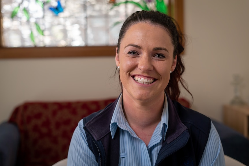 A woman with long brown hair wearing a blue shirt and a vest