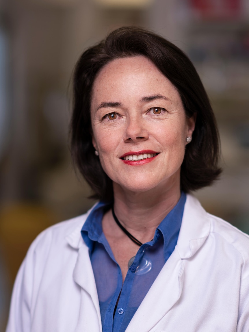 Head shot of a woman wearing a white lab coat in a scientific laboratory.