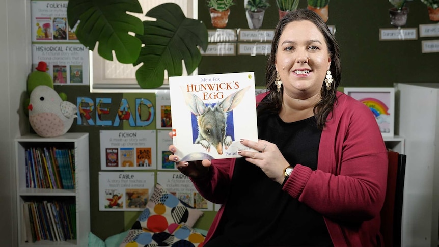 Female teacher holds up book titled "Hunwick's Egg"