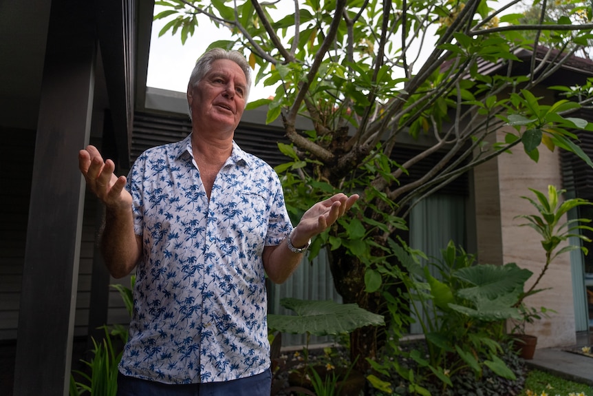 A man with grey hair in a tropical shirt gesticulates while talking 