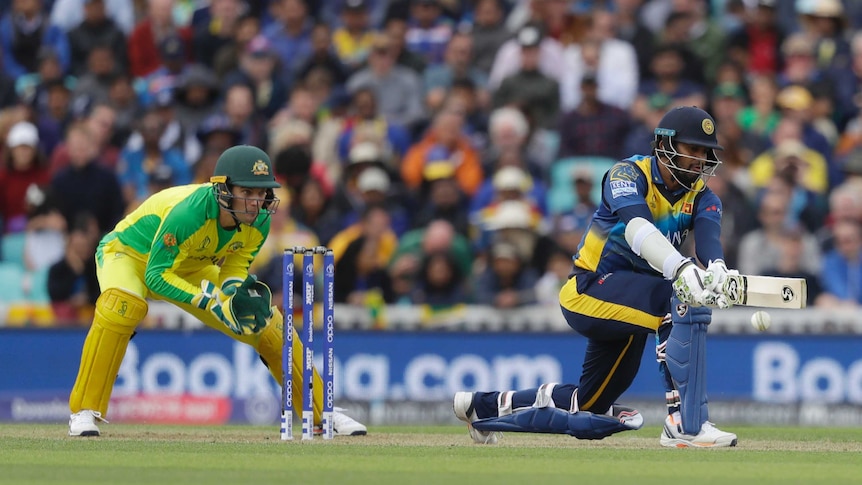 Dimuth Karunaratne plays a reverse sweep shot on one knee as Alex Carey crouches behind the stumps