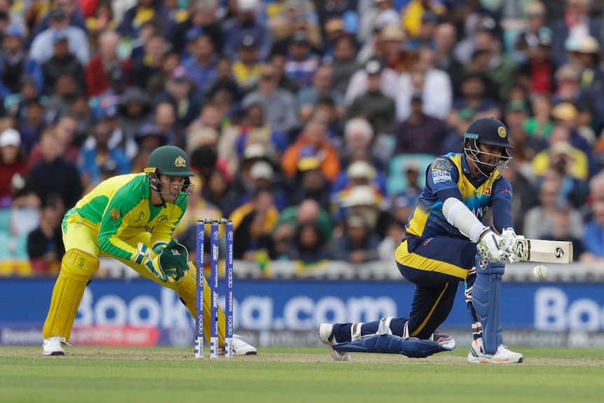 Dimuth Karunaratne plays a reverse sweep shot on one knee as Alex Carey crouches behind the stumps