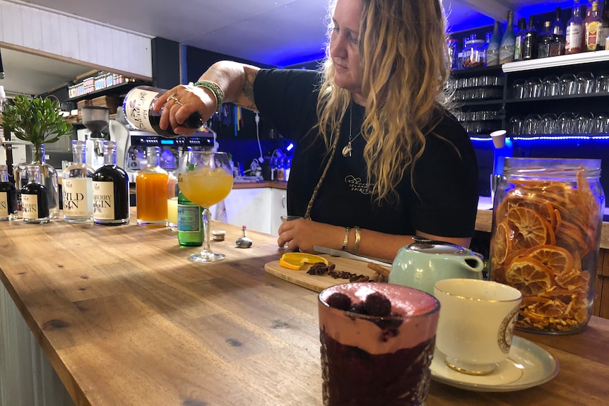 A woman with blond hair pouring mulberry gin into a cocktail.