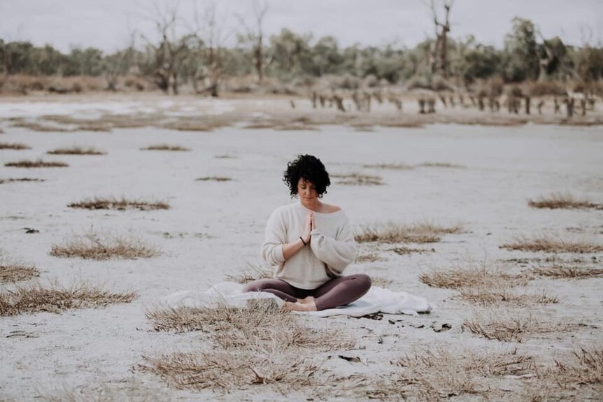 Jade Malinovski sits on a floodplain in a yoga pose.