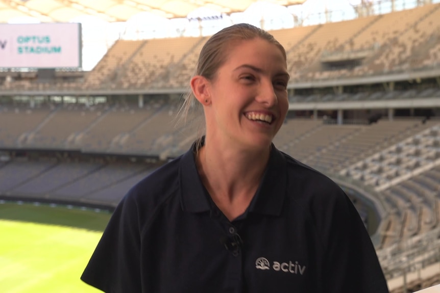 A woman in a dark polo shirt smiling in a sports stadium