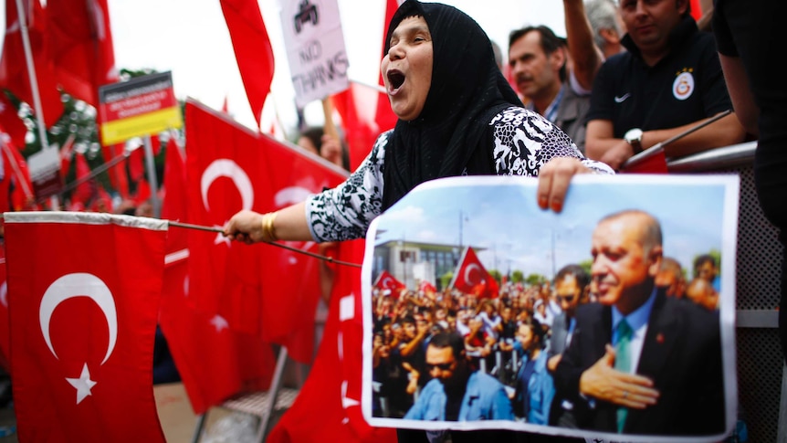 A woman yells while holding a picture of Turkish President Tayyip Erdogan and a Turkish flag.