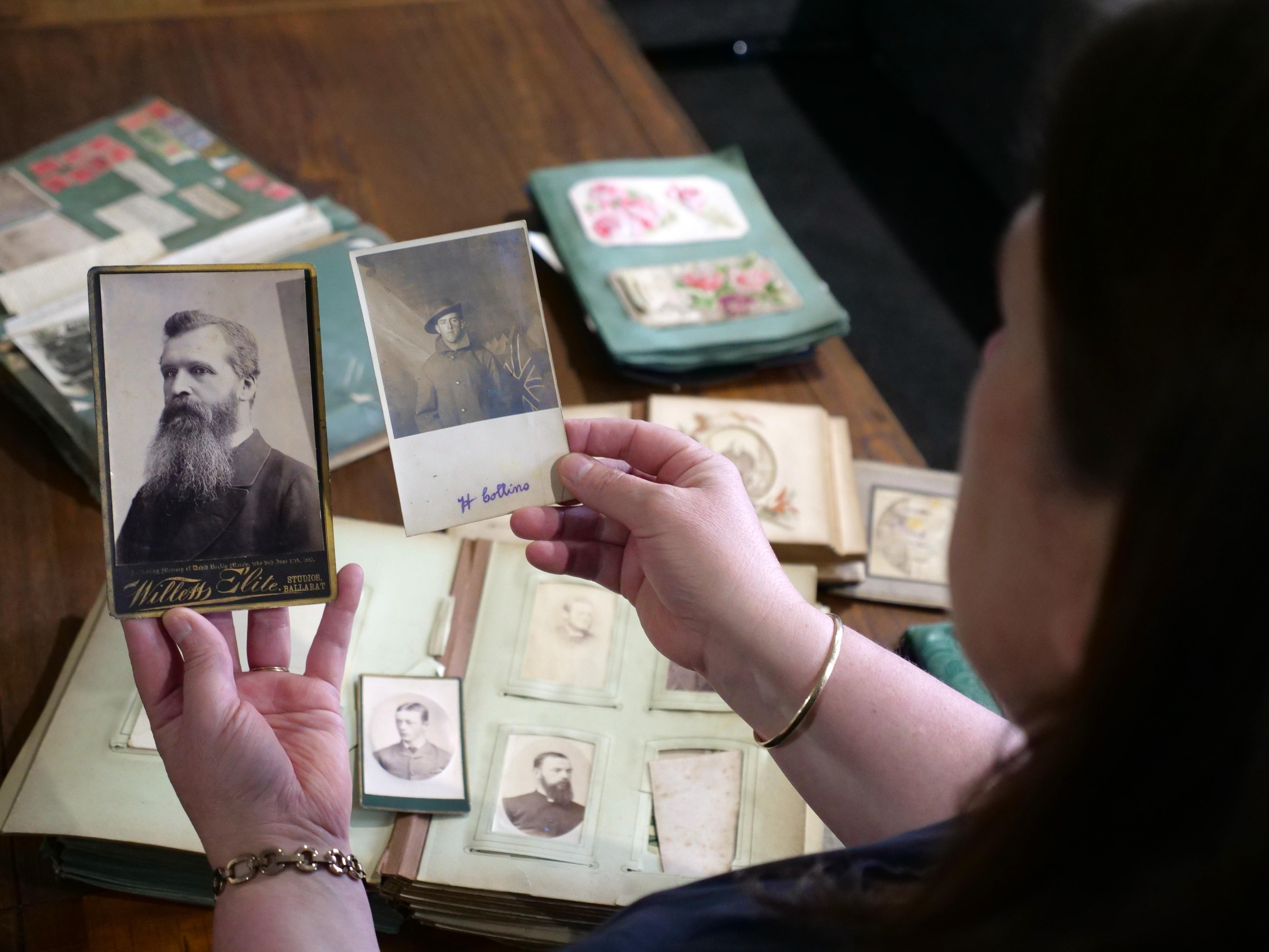 A woman holds two historic photos with photo albums in the background on the table
