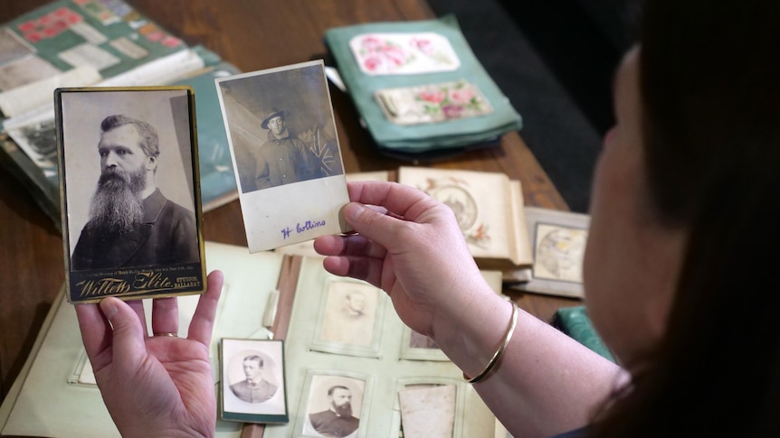A woman holds two historic photos with photo albums in the background on the table