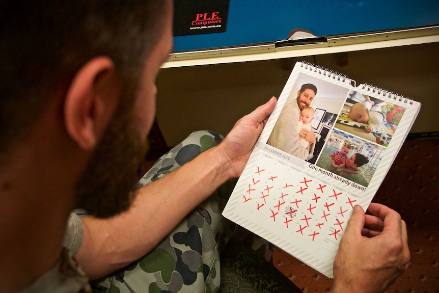 He is holding a calendar with photos of his family and dates marked with red crosses.