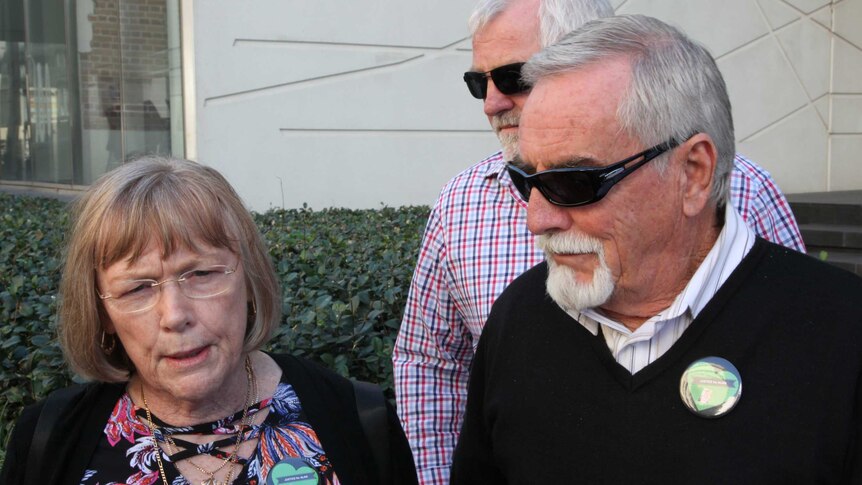 A woman in glasses and a man in sunglasses talk to the media outside the court building.