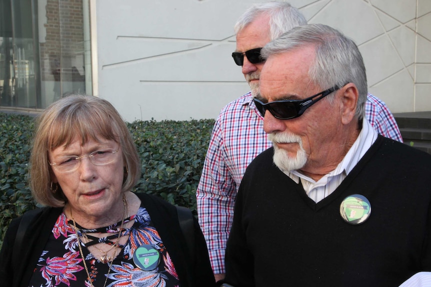 A woman in glasses and a man in sunglasses talk to the media outside the court building.