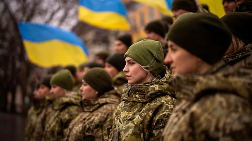 Ukrainian Army soldiers pose for a photo in front of national flags