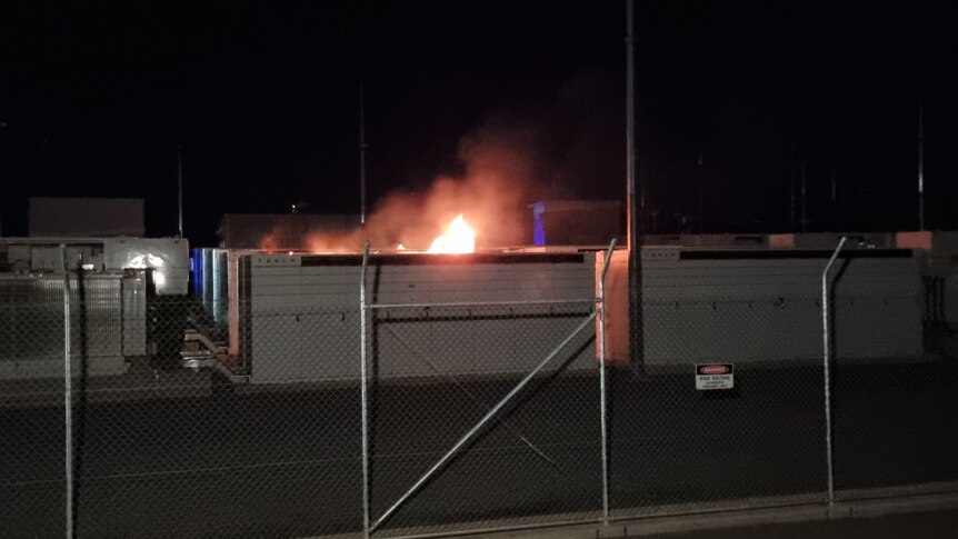 Flames above a large battery box behind a fence at night time