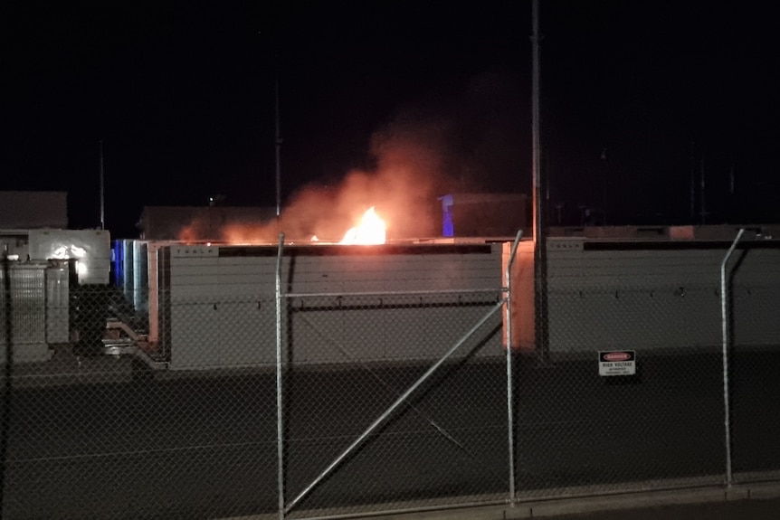 Flames above a large battery box behind a fence at night time