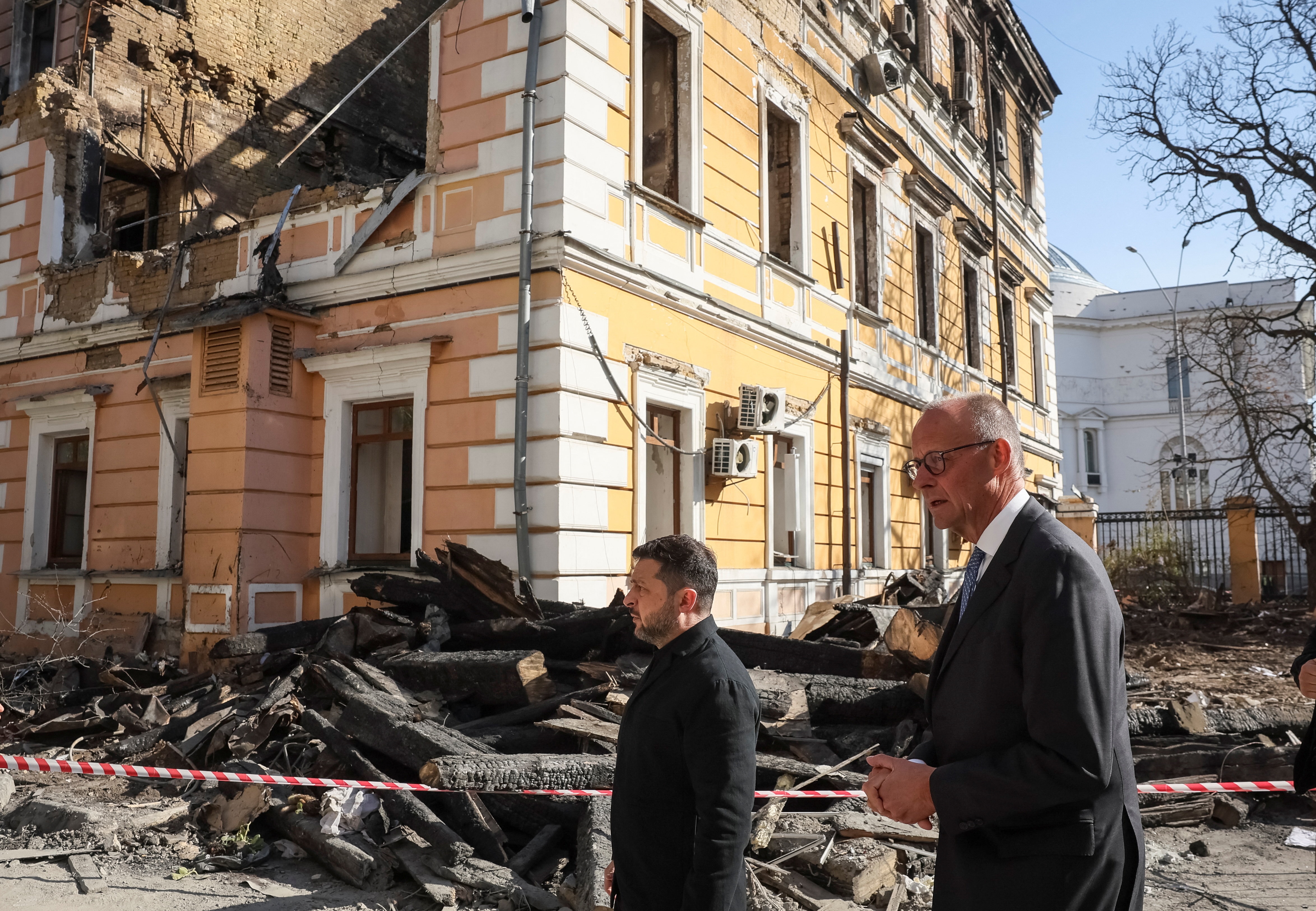 Volodymyr Zelenskyy (left) and Friedrich Merz stand outside a building, damaged by a drone strike.