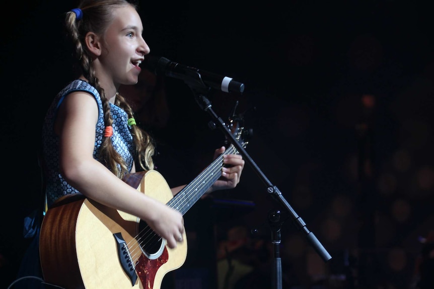 A girl singing while holding a guitar