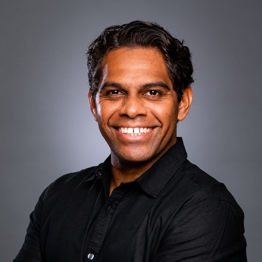 Young man in black shirt, arms folded, smiling at the camera.