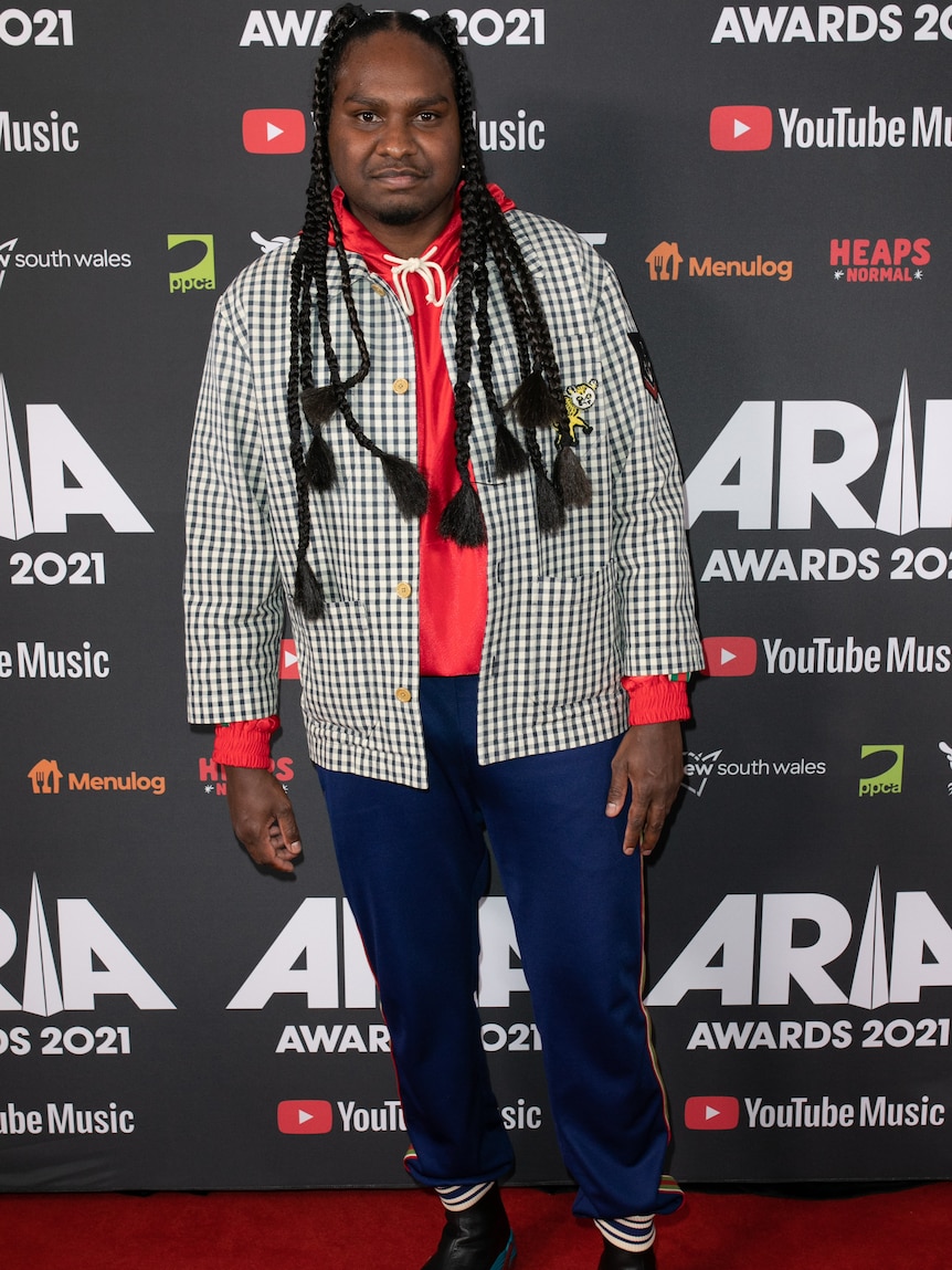 A man in a red shirt, check jacket and blue jeans on red carpet.