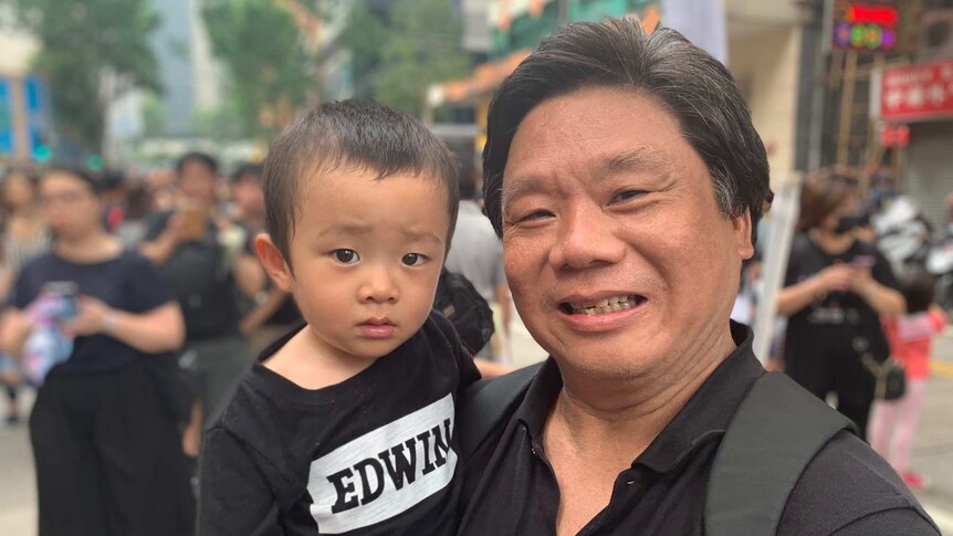 A man holding his grandson smiles at the camera