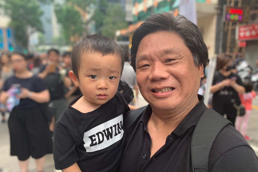 A man holding his grandson smiles at the camera