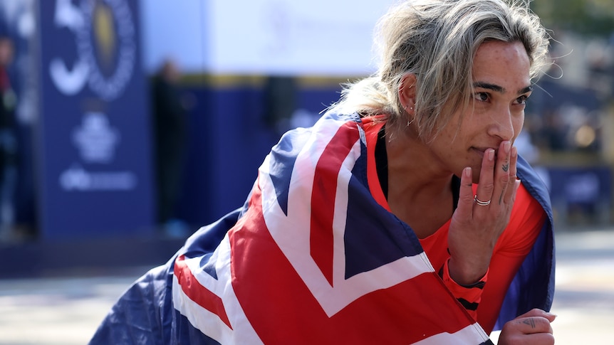 Madison de Rozario holds her hand to her mouth draped in a Australia flag