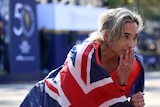 Madison de Rozario holds her hand to her mouth draped in a Australia flag